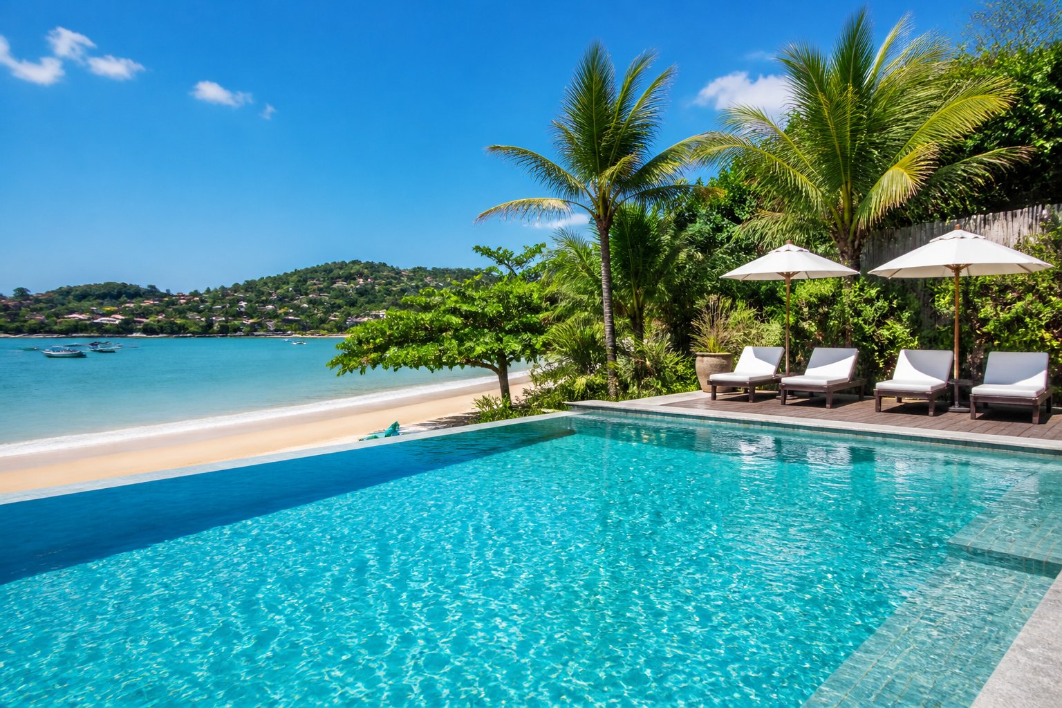 Piscina limpa e cristalina próxima a uma praia com areia, ondas suaves e vegetação tropical ao fundo.